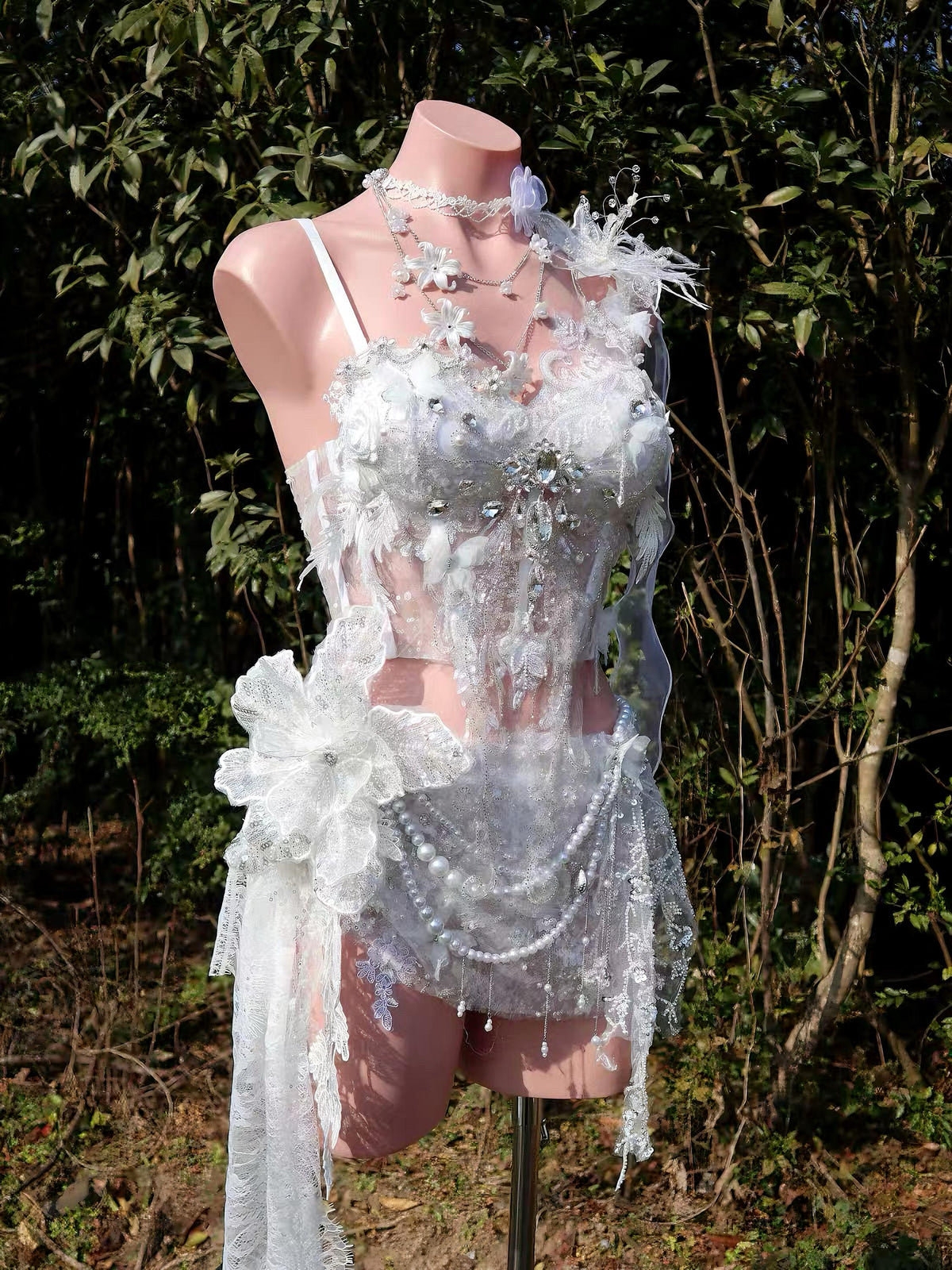 Ethereal white lace bodysuit with floral appliqués, pearls, and crystal embellishments on mannequin outdoors